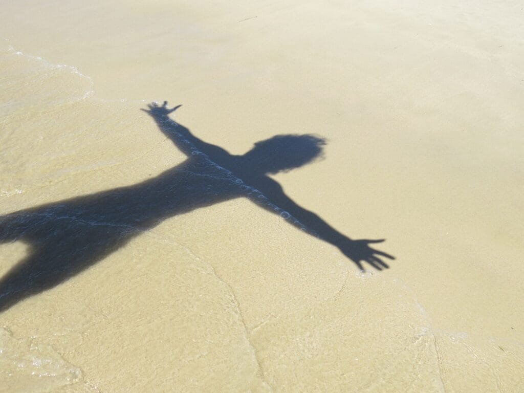 5 Formas do Estoicismo Melhorar Sua Saúde Mental 4 sombra na areia da praia de um homem de braços abertos