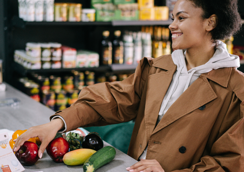 mulher negra sorrindo passando legumes no caixa